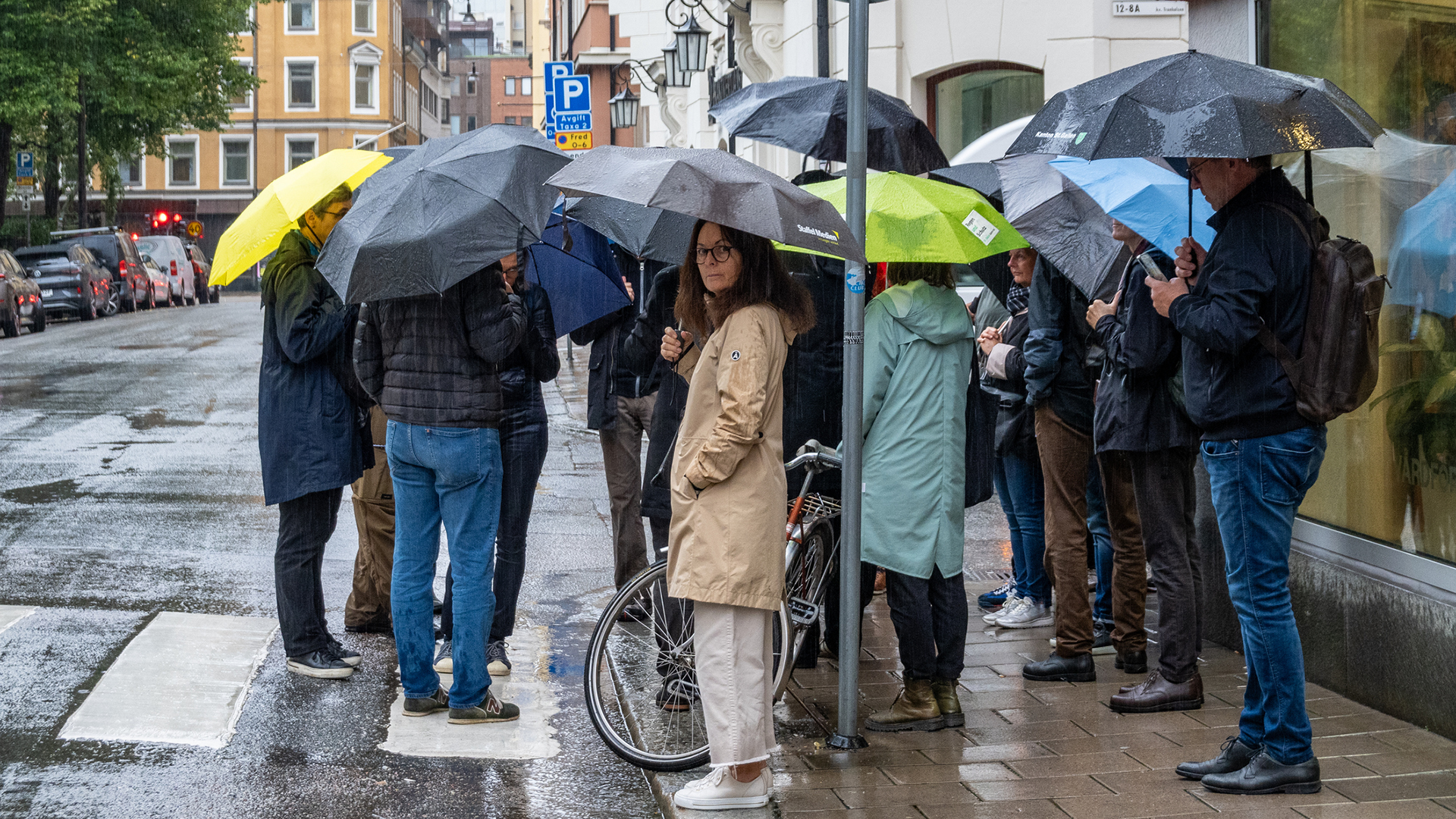 En grupp personer står i en klunga under paraplyer i stadsmiljö