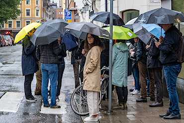 En grupp personer står i en klunga under paraplyer i stadsmiljö