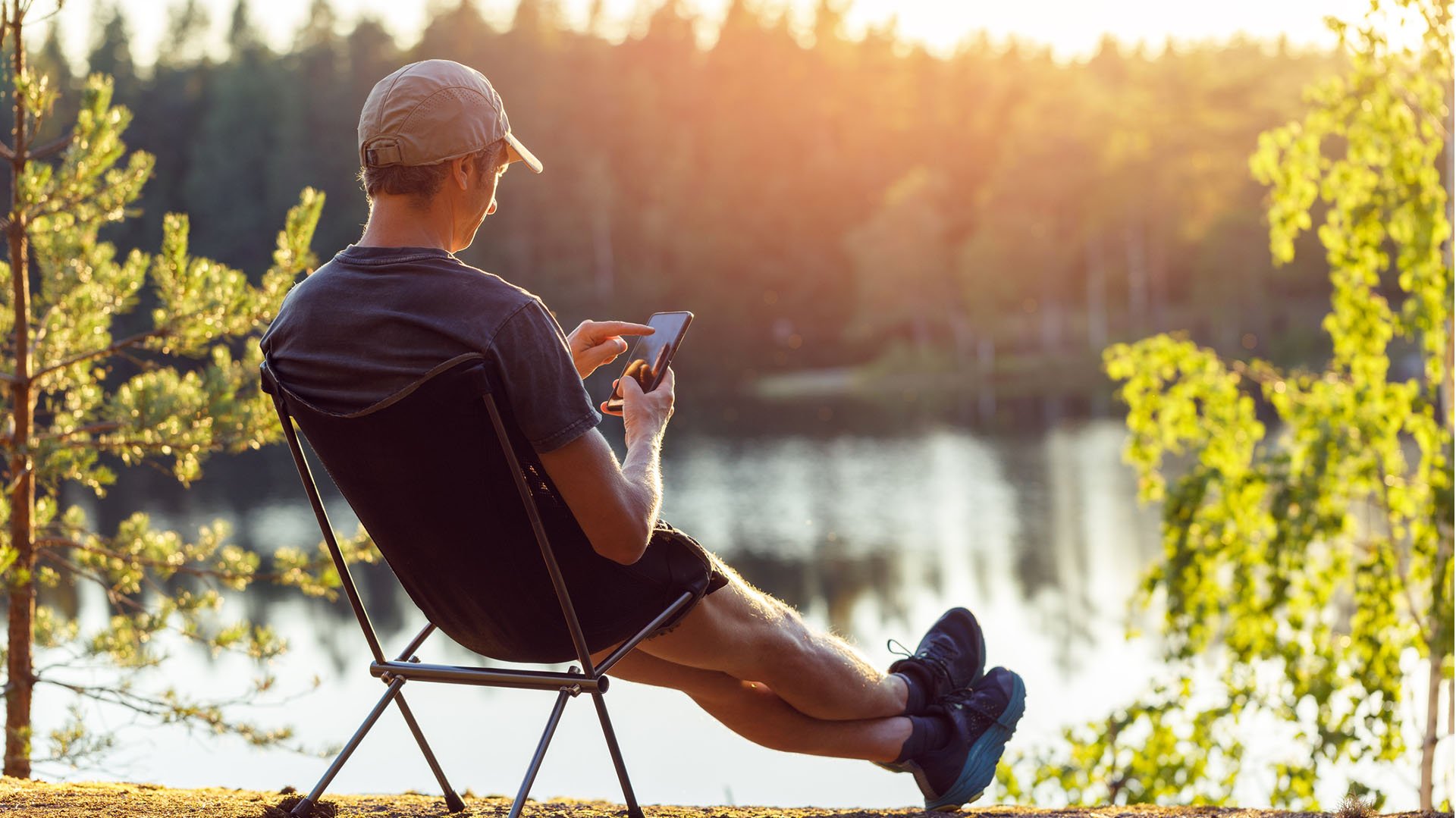 Person sitting in a chair by a lake and checking his mobile phone