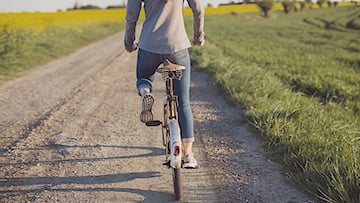Kvinna cyklar på grusväg vid åker