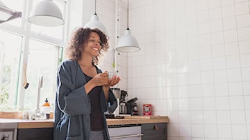 Kvinna lutar sig mot diskbänken med kaffekopp i handen